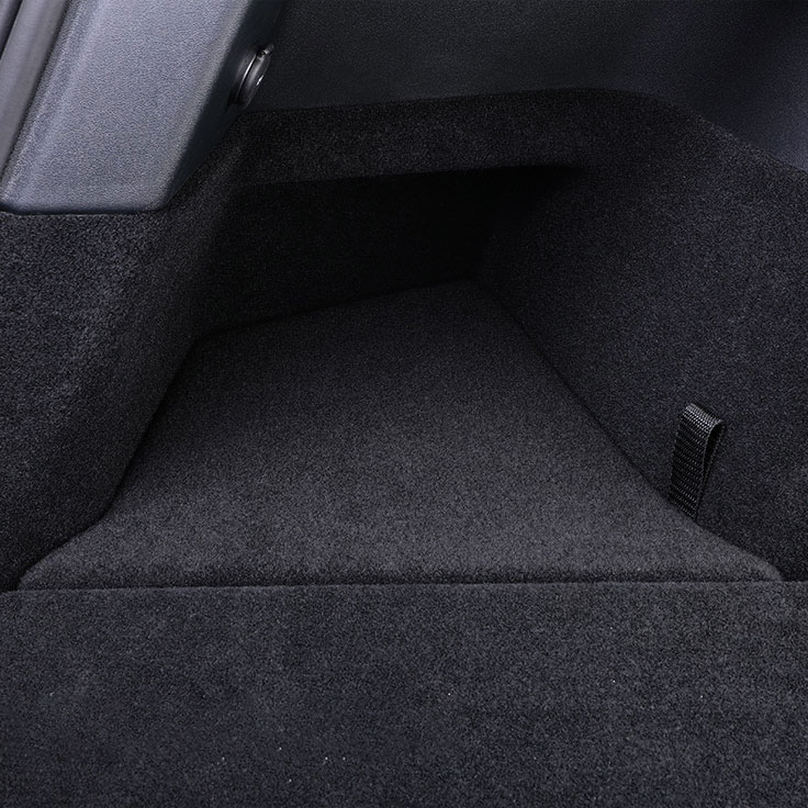 Empty car trunk lined with dark carpet; side panel visible on left and a fabric loop on the right for securing cargo.