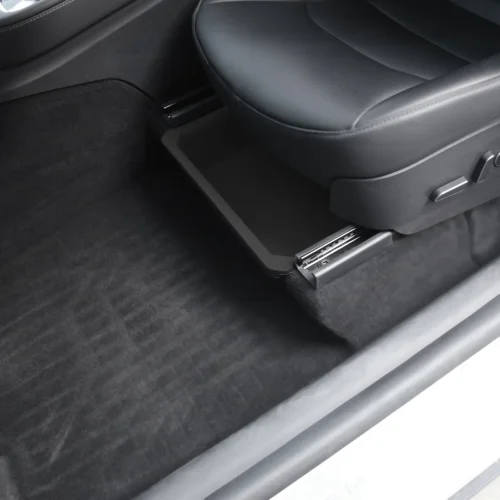 Open slide-out storage tray under the front car seat in a dark interior, showing a black plastic drawer extending from the seat base.