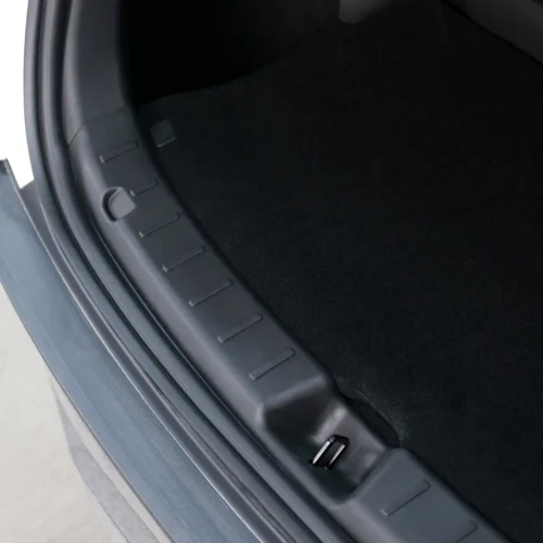 Close-up of a car trunk opening showing a black plastic sill plate along the edge and a small latch at the bottom.