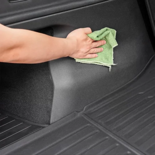 Person cleaning the car’s interior floor with a green microfiber cloth.