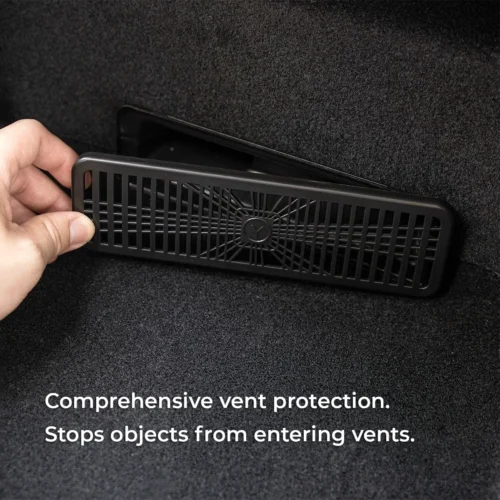 Hand inserting a protective vent cover to block debris from a car trunk vent in a dark carpeted surface; automotive accessory.