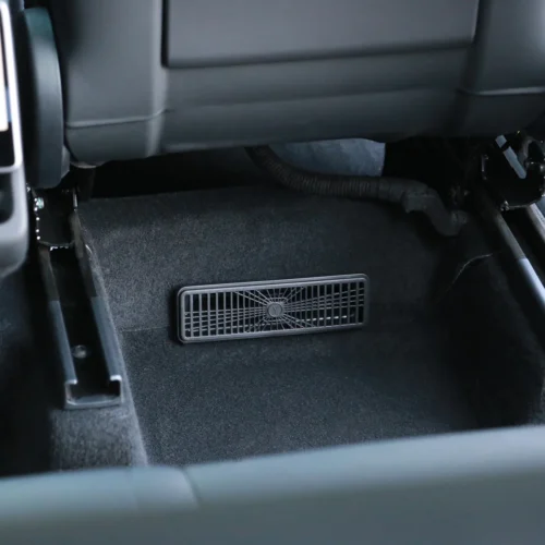 Rectangular air vent grille mounted in the front car floor between the seats.