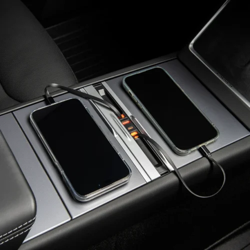 Two smartphones resting in a car's center console charging dock with cables connected and orange indicator lights showing.