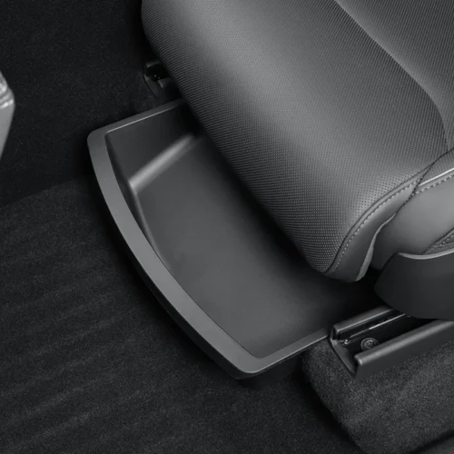 Under-seat storage tray pulled out next to a gray car seat on a black carpeted floor.