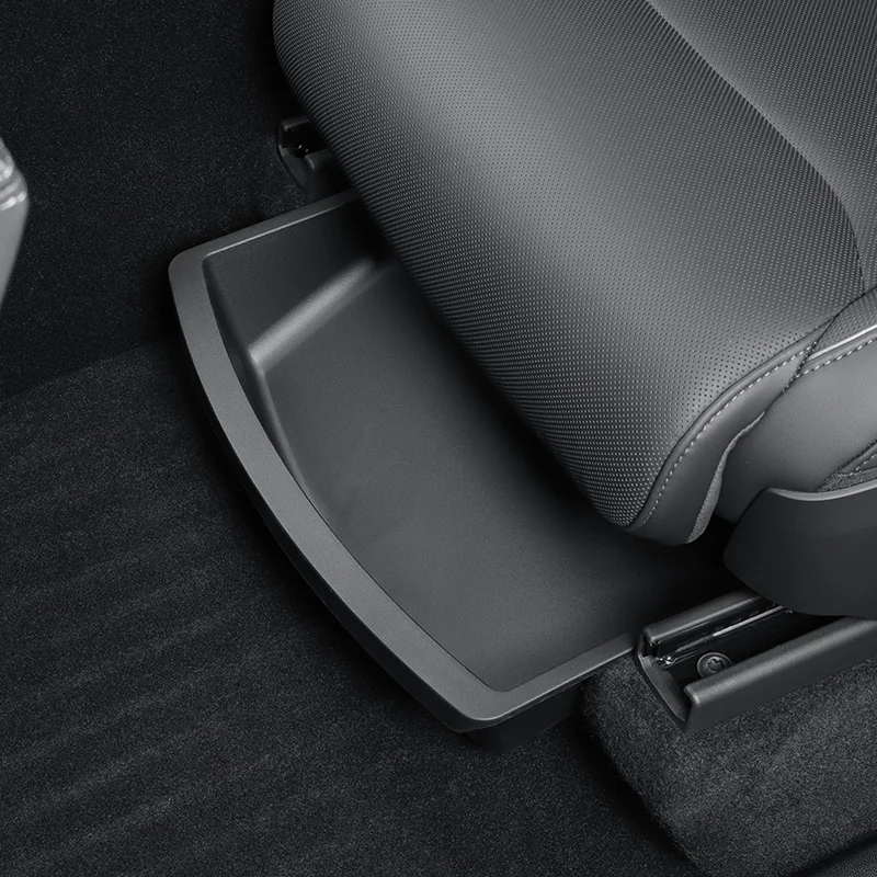 Under-seat storage tray pulled out next to a gray car seat on a black carpeted floor.