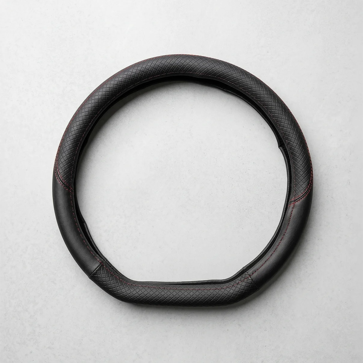Black textured leather steering wheel cover with red stitching, laid flat as a circular ring on a light gray surface.