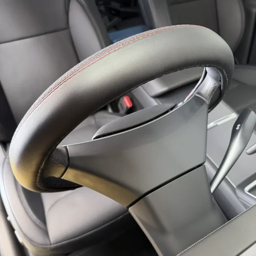 Close-up of a car steering wheel with red contrast stitching and leather grip.