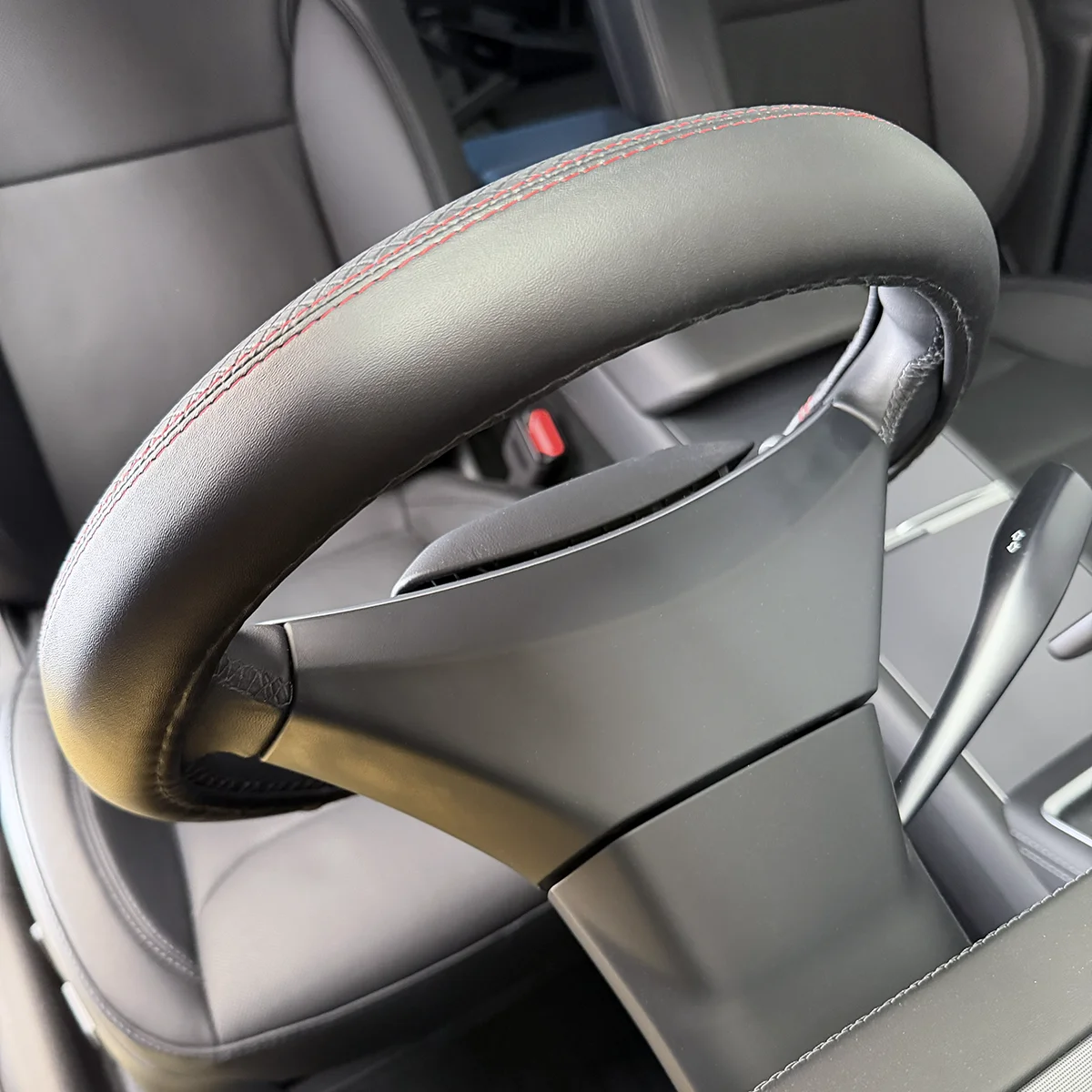 Close-up of a car steering wheel with red contrast stitching and leather grip.