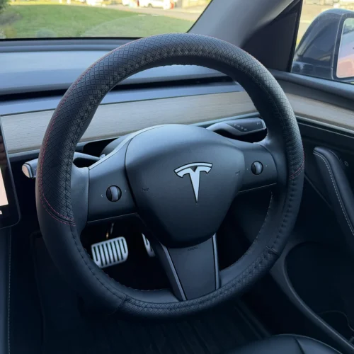 Tesla steering wheel wrapped in quilted leather with red stitching inside a car cabin