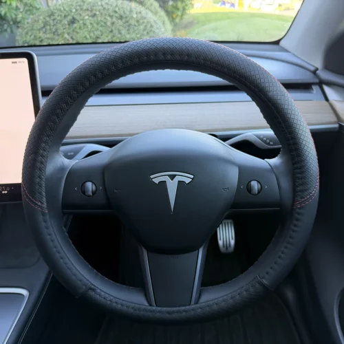 Tesla steering wheel with a textured black cover and red stitching inside a car cabin.