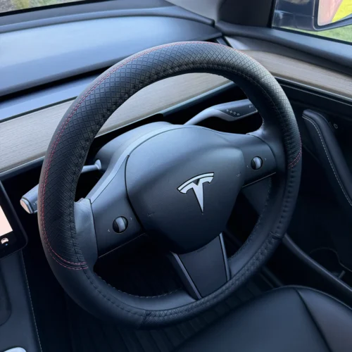 Tesla steering wheel with a black textured cover and red stitching inside a modern car interior.