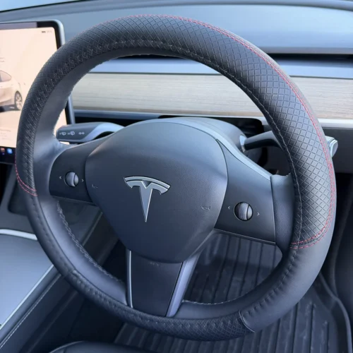 Close-up of a black leather Tesla steering wheel with red contrast stitching and satin trim.