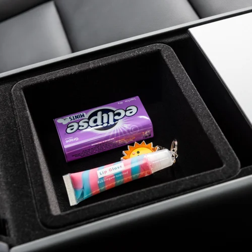 Center console storage tray with a purple Eclipse mints tin, a colorful lip gloss tube, and a sun-shaped keychain visible for a casual car interior scene.