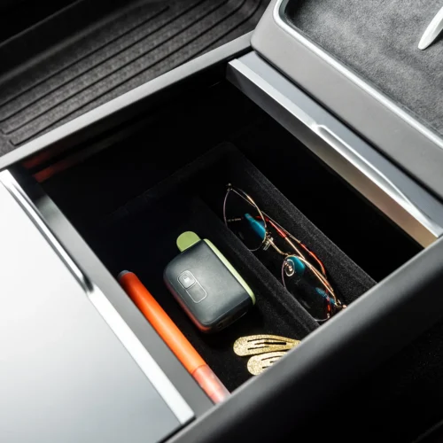Open car center console drawer with sunglasses, a car key fob, an orange pen, and gold hair clips inside.