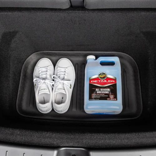 White sneakers and a blue bottle of Meguiar's Detailer All Season Dressing in a car trunk storage tray.