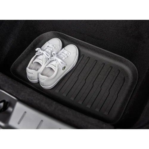 A pair of white Lacoste sneakers inside a car trunk on a black ribbed cargo mat