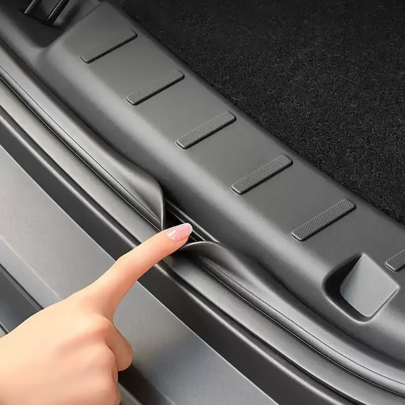 Finger lifting the plastic trunk sill trim along a car's rear edge to access the cargo area.