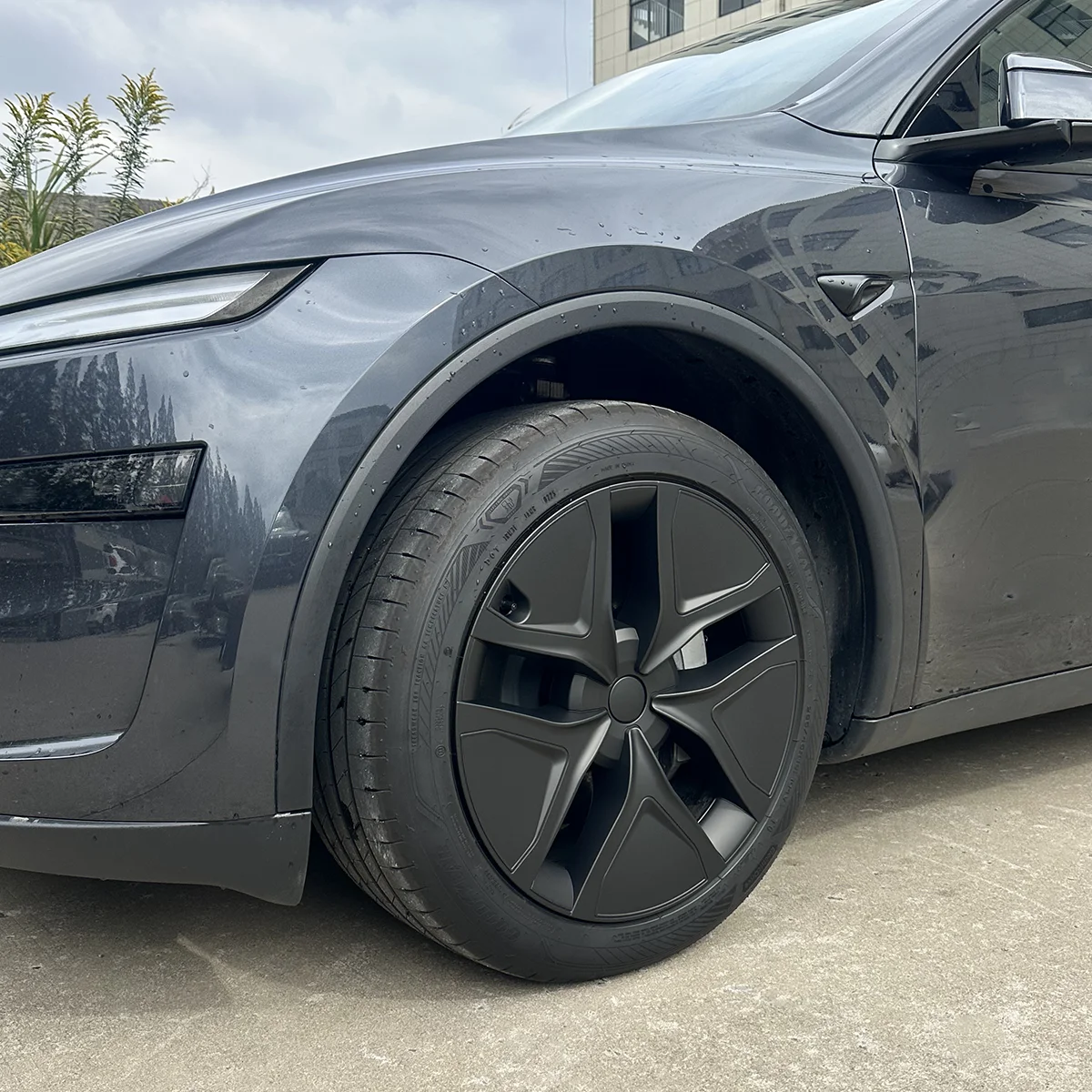 Close-up of a dark gray car's front left wheel and fender, showing an aerodynamic wheel design.
