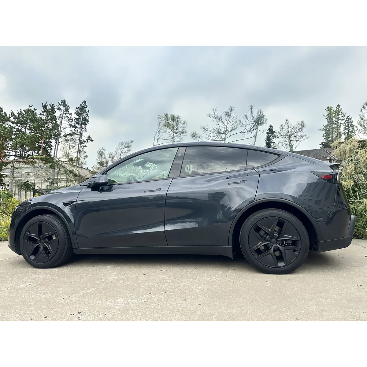 Side view of a dark gray electric crossover SUV parked on a driveway with trees in the background.
