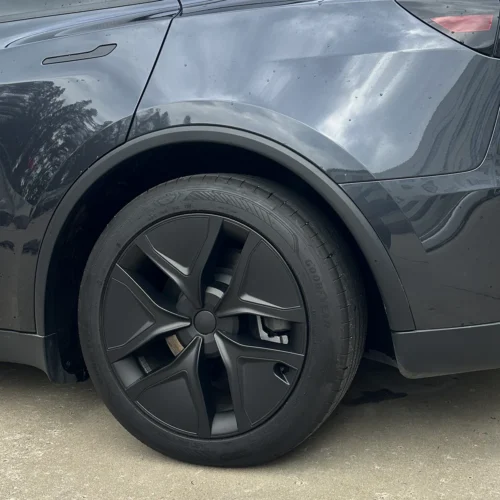 Close-up of a dark gray car's front left wheel with a black multi-spoke alloy rim and a Goodyear tire visible in the wheel well.