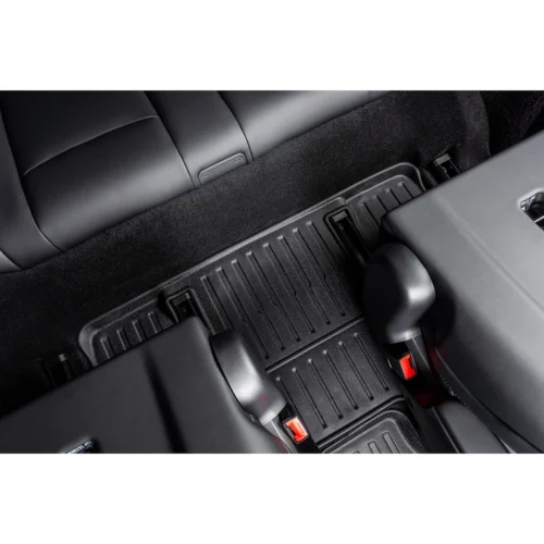 Back seat floor area of a car with black ribbed rubber floor mats and red seat belt buckles visible at the seat edges.
