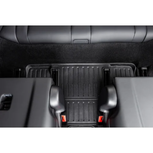 View from above of a car's rear passenger area showing a ribbed black floor mat and two seat bases with red seatbelt latches on either side