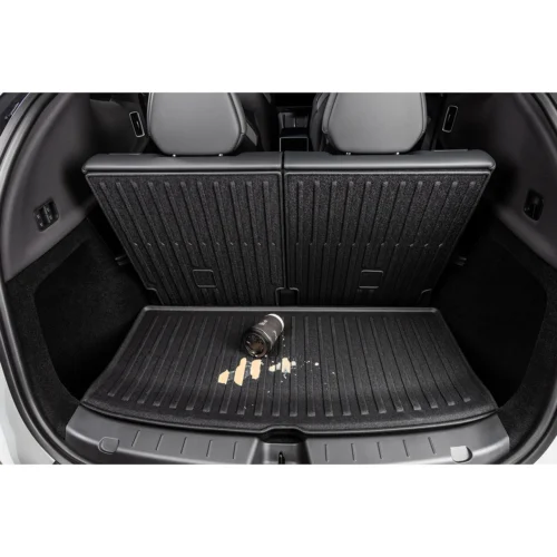Car trunk with back seats up; a coffee cup spilled on the ridged cargo mat in the floor area.