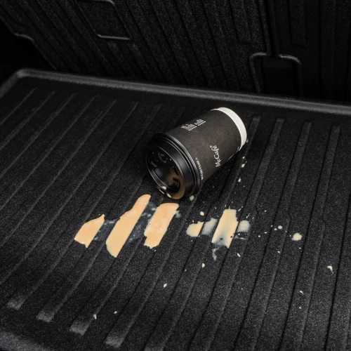 McCafé disposable cup tipped over on a truck bed liner with spilled beige liquid nearby.