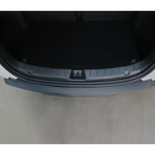 Open car trunk viewed from above, showing a black cargo mat and a plastic scuff plate along the edge with a centered latch.