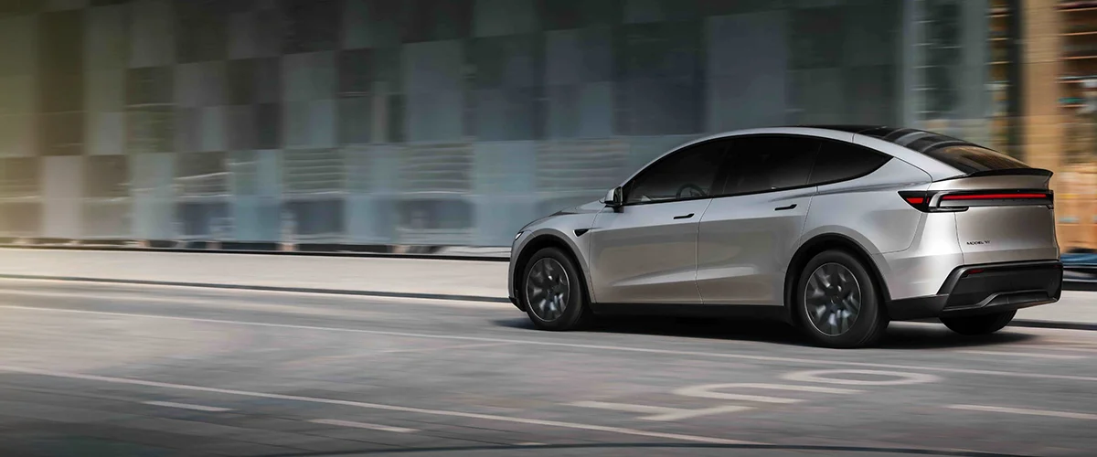 Silver SUV driving past a glass-fronted building on an urban street, side view in motion